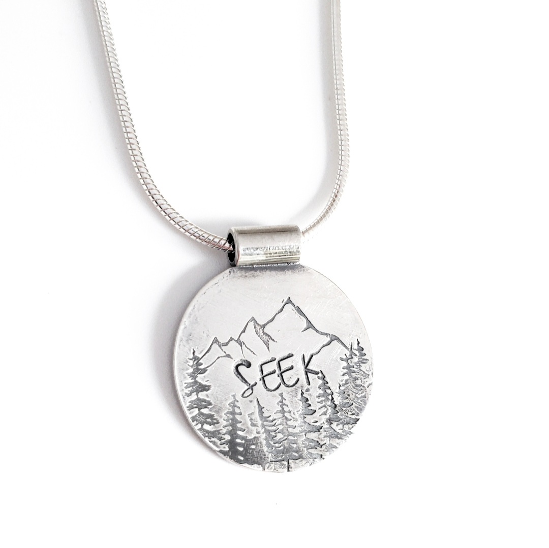 Sterling silver pendant necklace stamped with mountains, trees, and the word SEEK