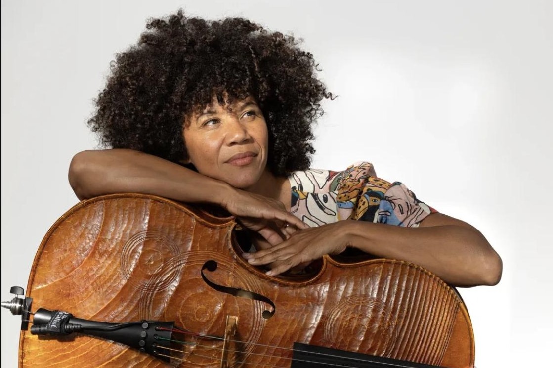 Portrait of a cellist resting her arms on her cello, smiling